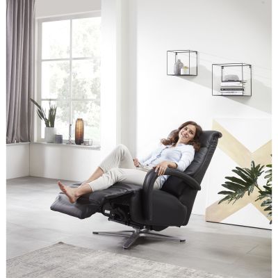 Frau entspannt in einem schwarzen Relaxsessel mit hochgeklappter Fußstütze im Wohnzimmer