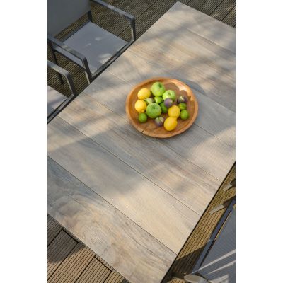 Nahaufnahme einer Tischplatte in Holzoptik mit natürlicher Maserung und Schatten von Pflanzen im Sonnenlicht.