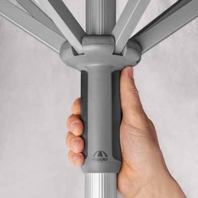 Nahaufnahme einer Hand, die den ergonomischen Griff am Mast des hellgrauen Sonnenschirms betätigt, stabile Streben sichtbar.