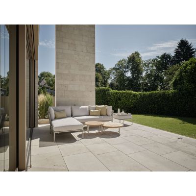 Sitzgruppe mit gepolsterten Sitzmöbeln und runden Tischen auf einer Terrasse vor einem Gebäude mit angrenzender Grünfläche