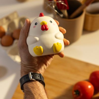 Weiße Antistress-Figur in Hühnerform, in einer Hand über einer Küchenarbeitsfläche zusammengedrückt gezeigt.
