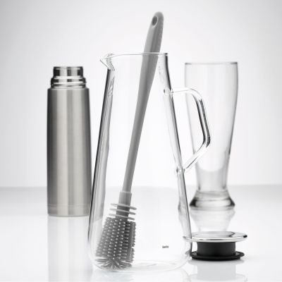 Lichtgraue Flaschenbürste auf einer Arbeitsfläche neben Flasche und Gläsern