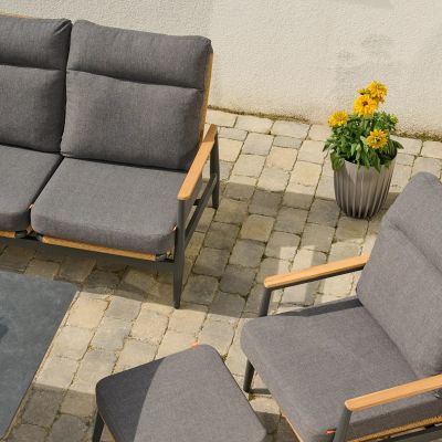 Blick von oben auf ein Sofa und einen Sessel mit grauen Polstern, daneben ein Hocker, im Hintergrund gelbe Blumen in einem Pflanztopf.