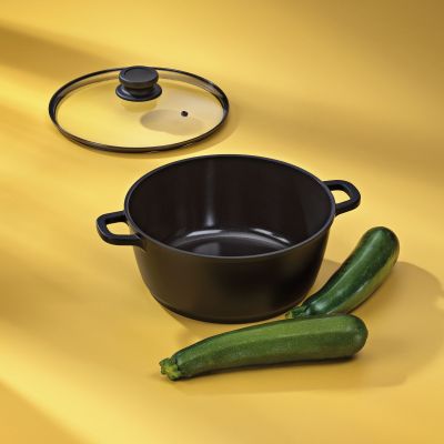 Geöffneter schwarzer Fleischtopf ohne Deckel neben zwei Zucchini und abgelegtem Glasdeckel