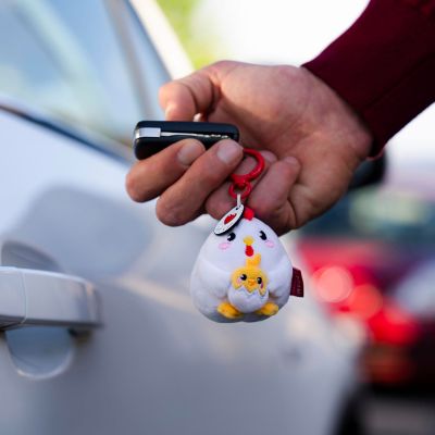 Hühner-Plüsch-Schlüsselanhänger, an einem Schlüsselbund neben einer Autotür gehalten gezeigt.