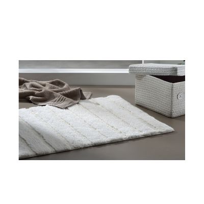 Längliche offwhite Megan-Badematte auf hellem Boden mit grauem Korb und beigefarbenem Handtuch im Hintergrund.