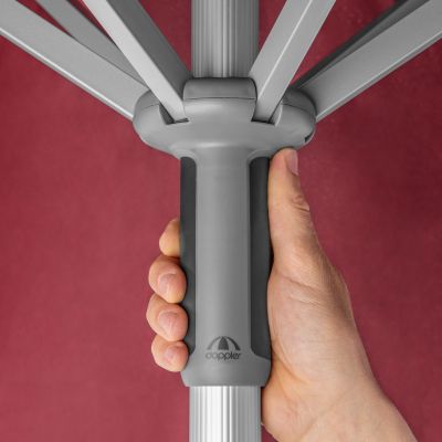 Hand hält den ergonomischen Griff am Mast des roten Sonnenschirms, stabile Streben und doppler-Logo sichtbar.