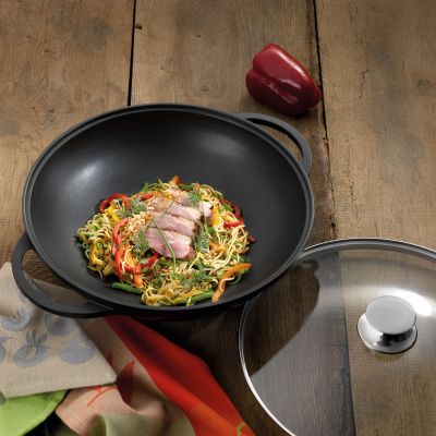 Schwarzer Wok mit Gemüsegericht auf einer Arbeitsfläche neben einem Glasdeckel