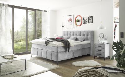 Graues Boxspringbett im eingerichteten Schlafzimmer, dekoriert mit Kissen und Decke, präsentiert in wohnlichem Ambiente