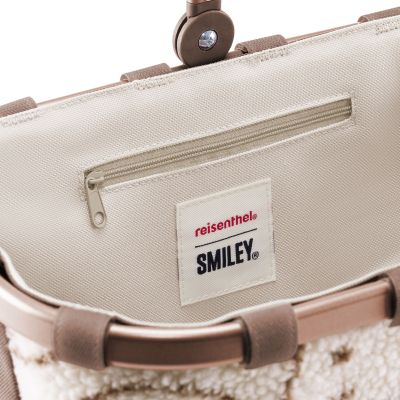 Kleiner Einkaufskorb von Reisenthel, Modell Carrybag XS, in Creme und Braun mit Smiley-Muster aus Teddyfleece, Nahaufnahme des inneren Reißverschlussfachs mit Smiley-Logo