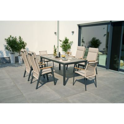 Mehrere Stühle mit beige-grauen Polstern stehen um einen großen rechteckigen Tisch auf einer Terrasse, im Hintergrund Pflanzen und eine Glasfassade.