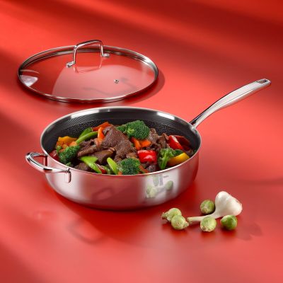 Edelstahl Schmorpfanne mit Glasdeckel und Gemüsefüllung auf rotem Hintergrund neben kleinen Tomaten