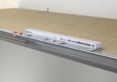Eine silberfarbene Metallleiste ist auf einer Holzplatte montiert und mit Schrauben befestigt, im Hintergrund sind Teile eines Möbelstücks sichtbar