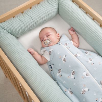 Schlafendes Baby im hellblauen Schlafsack mit Tiermotiv in einem Babybett