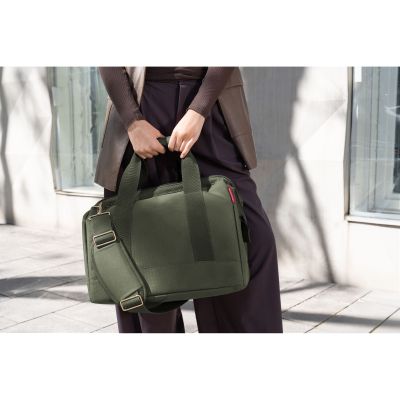 Reisetasche von Reisenthel, Modell Allrounder M, in Olivgrün mit goldfarbenen Beschlägen, von einer Person an den Tragegriffen getragen
