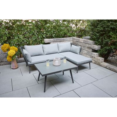 Gartenlounge mit Ecksofa und Tisch auf einer Terrasse im Garten mit Hecke und Steinmauer im Hintergrund