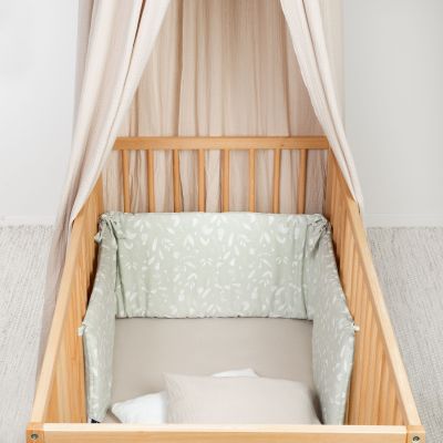 Holz-Babybett mit olivgrünem Nestchen mit weißem Blättermuster und beigem Baldachin, innen mit Kissen und Decke ausgestattet