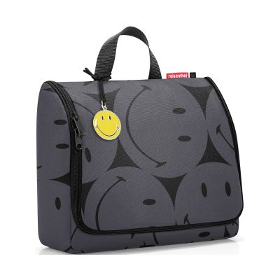 Kulturbeutel von Reisenthel, Modell Toiletbag XL, in Grau mit großflächigem Smiley-Muster, schräg von vorn geschlossen mit Tragegriff und Smiley-Anhänger.