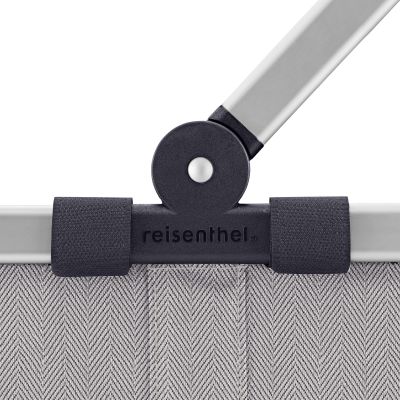 Einkaufskorb von Reisenthel, Modell Carrybag, in Hellgrau mit feinem Fischgrätmuster, als Nahaufnahme des Gelenks zwischen Aluminiumgriff und Korbrand.