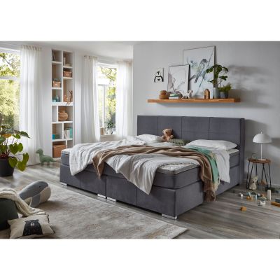 Boxspringbett mit grauem Stoffbezug und Bettwäsche in einem eingerichteten Schlafzimmer