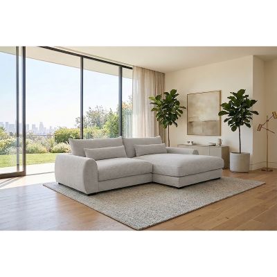 Milieubild eines weißen Ecksofas mit rechter Ottomane, breiten Armlehnen und schwarzen Kunststofffüßen in einem Wohnzimmer mit großen Fensterflächen
