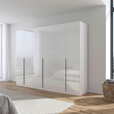 Moderner weißer Hochglanz Drehtürenschrank mit sechs Türen und grau-metallicen Griffen in einem hellen Schlafzimmer mit großen Fenstern