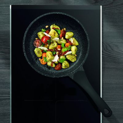 Bratpfanne mit Paprika Zucchini und weiterem Gemüse auf einem dunklen Kochfeld aus der Draufsicht
