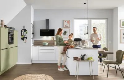 Junge Familie mit kleinem Mädchen entspannt in einer klassischen L-Küche Interliving Serie 3071 in Arcticweiß, Avocado softmatt und Eiche Graphitsilber