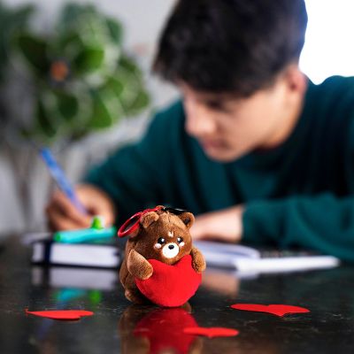 Brauner Teddybär-Plüsch-Schlüsselanhänger mit rotem Herz, vor einer sitzenden Person auf einem Schreibtisch dargestellt.