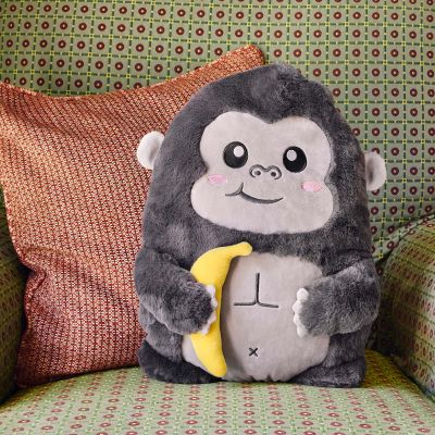 Graues Gorilla-Kissen mit gelber Banane, auf einem gemusterten Sofa neben einem orangefarbenen Kissen dargestellt.