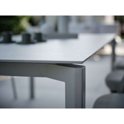 Nahaufnahme der Tischplatte eines rechteckigen Gartentisches mit glatter, heller Oberfläche und geradlinigem Tischbein, Umgebung unscharf dargestellt.