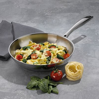 Edelstahl-Bratpfanne mit zubereitetem Gemüse, Kartoffeln und Tomaten auf einer grauen Arbeitsfläche