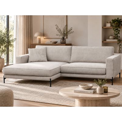 Das beige Ecksofa mit linker Liegefläche steht in einem wohnlich eingerichteten Raum mit Teppich, Couchtisch und warmen Holzelementen.
