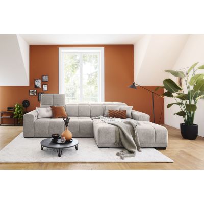Silbergraue Eckcouch mit Ottomane rechts im Bild, hochgestellter Kopfstütze, Zierkissen und Decke vor einer orangefarbenen Wand