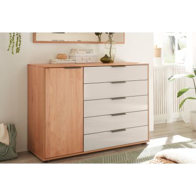 Kommode mit Tür links und fünf Schubladen rechts in heller Holzoptik mit hellen Fronten, aufgestellt in einem hellen Wohnraum neben Fenster und Pflanzen