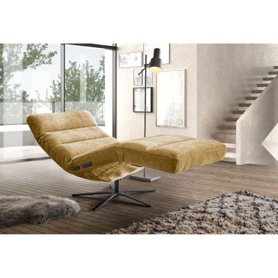 Relaxliege mit Bezug in Monty Pistaccio, nach hinten geneigter Rückenlehne, angehobener Beinauflage und schwarzem Sternfuß in einem hellen Wohnbereich mit Sofa, Teppich und Treppe