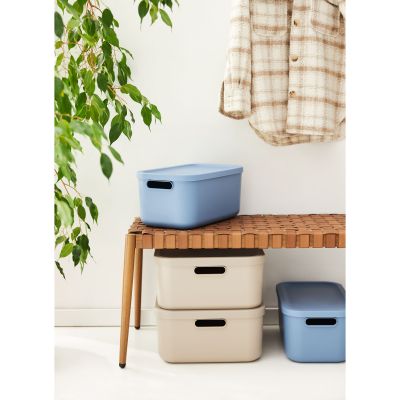 Blaue und beige Aufbewahrungsboxen aus Kunststoff neben einem Möbelstück im Wohnbereich