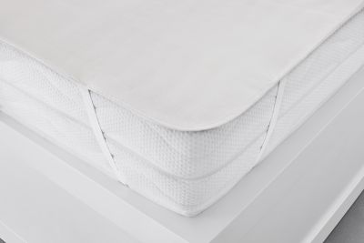 Nahaufnahme der Moltonauflage Luna in Creme an einer Matratzenkante; der seitliche Halt und die Stoffkante sind sichtbar; Größe 90 x 200 cm.