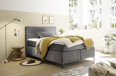 Boxspringbett „Voss 15 grey“ in einem eingerichteten Schlafzimmer, mit Kissen und Bettdecke ausgestattet, in wohnlichem Ambiente präsentiert