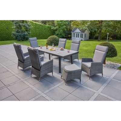 Mehrere Gartenstühle mit Polstern stehen um einen rechteckigen Tisch auf einer gepflasterten Terrasse im Garten