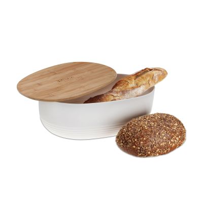 Ovaler weißer Brotkasten mit seitlich aufgelegtem Holzdeckel neben einem Brotlaib und geschnittenen Brotscheiben