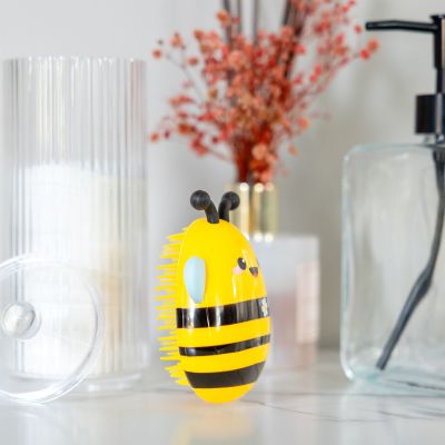 Haarbürste – Biene von Legami: Bienen-Haarbürste auf hellem Tisch vor einer Vase.