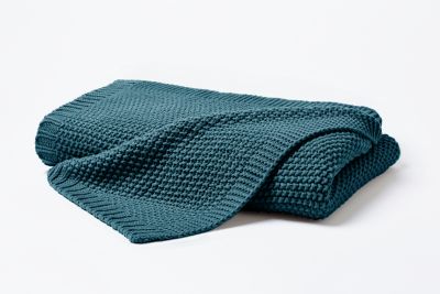 Gefaltete Strickdecke in Smaragd mit locker übergelegter Ecke; die grobe Waffelstrickstruktur ist vor hellem Hintergrund erkennbar; Größe 130 x 170 cm.
