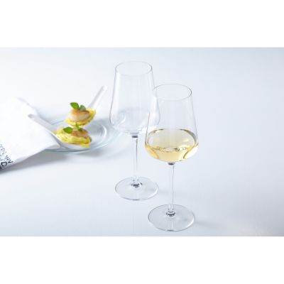 Zwei Weißweingläser eines gefüllt mit Weißwein auf hellem Tisch mit Dessert