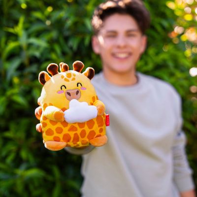 Orangefarbenes Giraffen-Plüschtier, von einer Person vor grünen Pflanzen gehalten gezeigt.