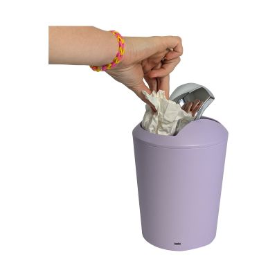 Eine Hand wirft kleinere Abfälle durch den geöffneten Schwingdeckel in den pastellvioletten Eimer