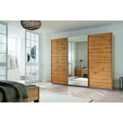 Schwebetürenschrank mit drei Türen, Korpus in Dekor Artisan Eiche und Front in Alu-Optik, mittlere Tür als Spiegelfront, aufgestellt in einem Schlafzimmer.