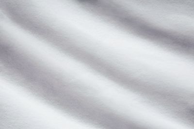 Nahaufnahme des Stoffes der Moltonauflage Luna in Creme mit feiner Oberfläche und sanften Wellen; Größe 90 x 200 cm.
