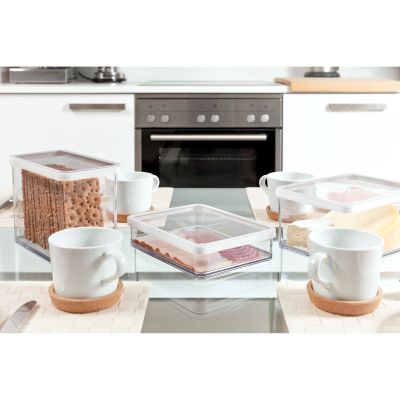 Transparente Vorratsdose mit Gebäck auf einem Tisch neben Geschirr und Getränken