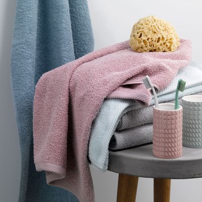 Altrosafarbenes Badtextil auf einem kleinen Beistelltisch neben Behältern Bürste und gelbem Badeschwamm